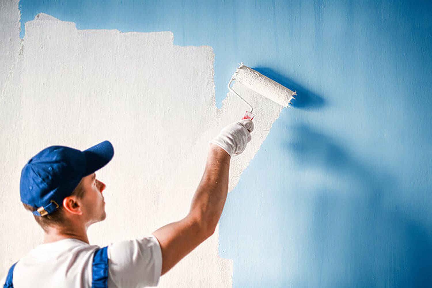 Professional painter rolling blue paint onto a large commercial wall interior.