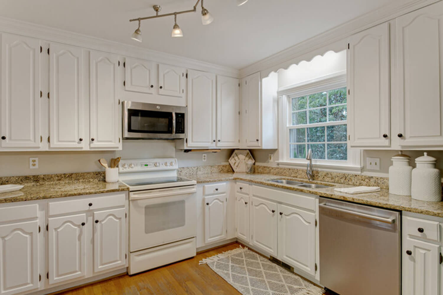 A kitchen with a full run of white cabinets, the type of dated but structurally sound cabinetry homeowners consider refinishing.