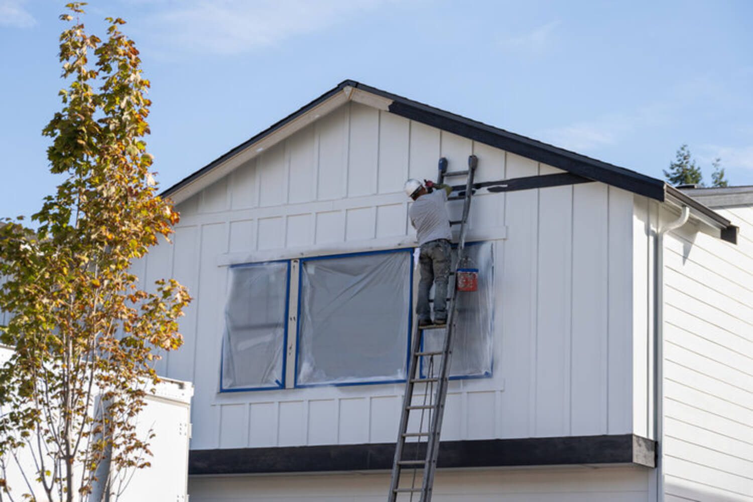 A painter working on a home's exterior siding in early fall, the type of project timing homeowners weigh before winter.