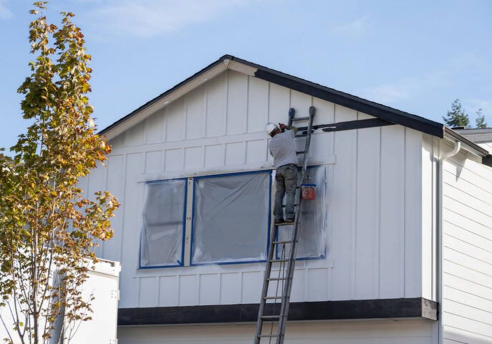 A painter working on a home's exterior siding in early fall, the type of project timing homeowners weigh before winter.