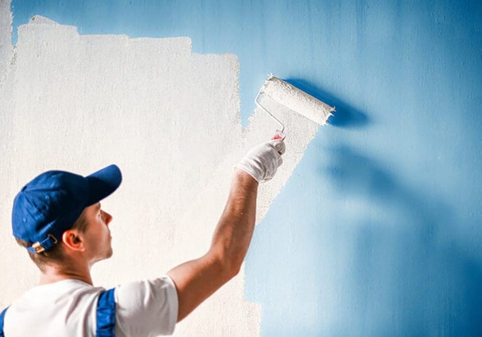 Professional painter rolling blue paint onto a large commercial wall interior.