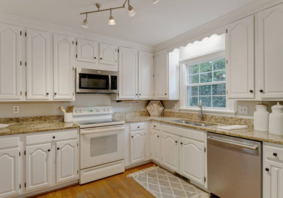 A kitchen with a full run of white cabinets, the type of dated but structurally sound cabinetry homeowners consider refinishing.