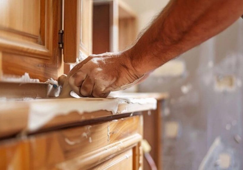 Painter sanding a wood cabinet surface as part of the professional cabinet refinishing process
