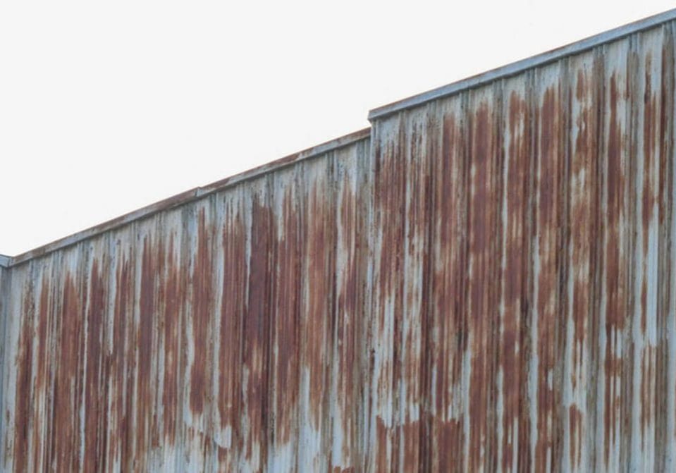 Rusted corrugated metal siding on an industrial facility showing signs of coating failure and corrosion